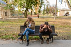 Pareja sentada en un parque mientras conversan, mostrando una conexión emocional negativa, relacionada con el manejo no saludable de los celos.